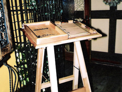 Massiv-Holz Gästebuch auf Ablage; Gegen Entwendung gesichert; Stativ kann als Rednerpult benutzt werden; Ablage und Vorrichtung für Beleuchtung (Klemmlampe) sind vorhanden